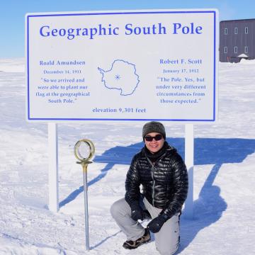 Howard Hui sits underneath a sign that says "Geographic South Pole" 