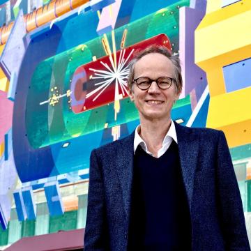 An image of Andreas Hoecker standing before a colorful wall